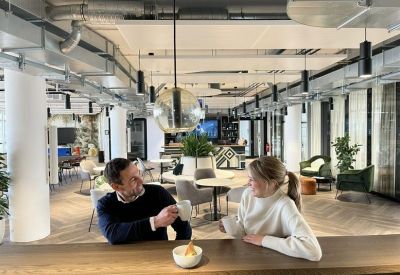 Bright breakout area featuring people talking at a wooden bar counter with hanging glass pendant lights.