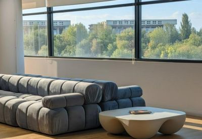 Bright breakout area featuring a long grey tufted sofa and a modern sculpted coffee table.
