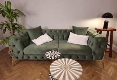 Green velvet tufted sofa with white cushions and patterned side tables on a herringbone wood floor.