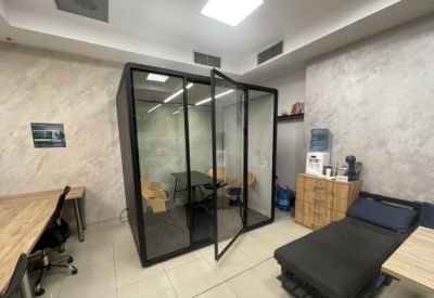 A standalone glass-walled meeting pod providing a private workspace within the open-plan office.