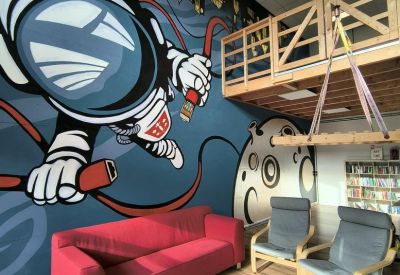 Coworking lounge with a red sofa and vibrant astronaut mural on a feature wall.