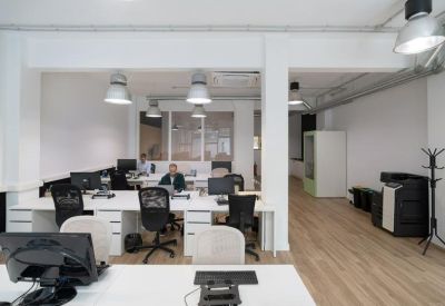 Bright office area with multiple workstations, black ergonomic chairs and wooden flooring.