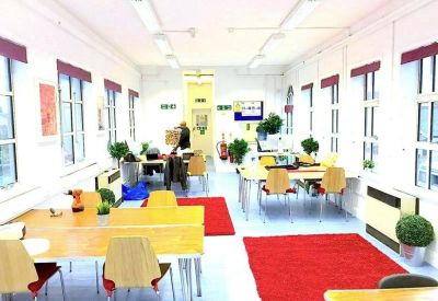 Spacious communal coworking area with large windows, red rugs, and wooden tables.