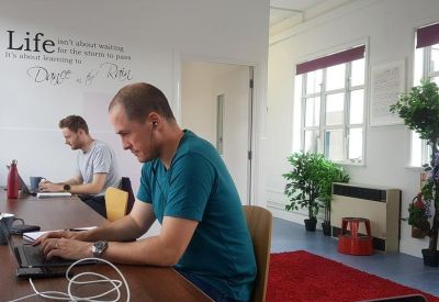 Man working on a laptop in a bright coworking space with whiteboard wall.