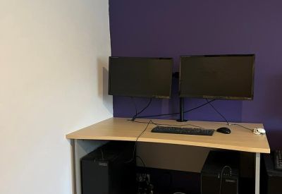 Modern dual-monitor workstation set against a vibrant purple accent wall with wooden flooring.