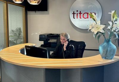 Curved wooden reception desk with a staff member on the phone in front of a branded wall logo.