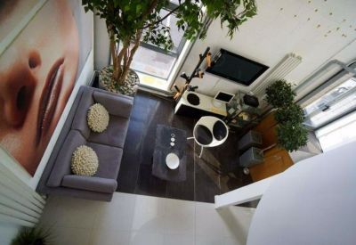 Aerial view of a bright communal lounge with a grey sofa, feature wall art, and indoor trees.