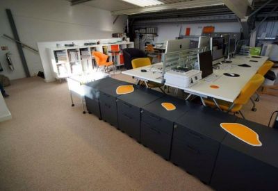 Open-plan office with white desks, orange chairs, and black storage units.