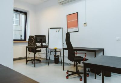 Functional two-person office with black desks, a whiteboard, and a small window.