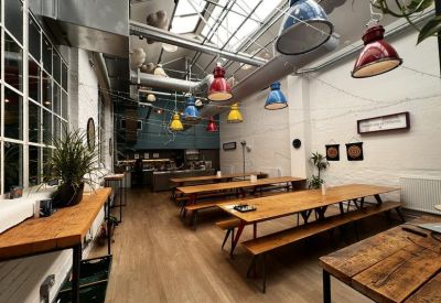 Spacious communal dining area with long wooden tables, benches, and colorful industrial pendant lights.
