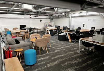 Open-plan office space featuring wooden desks, a grey sofa, and blue velvet ottomans.