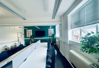 Bright coworking space with long white desks and a deep teal feature wall.