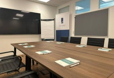 Spacious boardroom with a large wooden table, black chairs, and a monitor.
