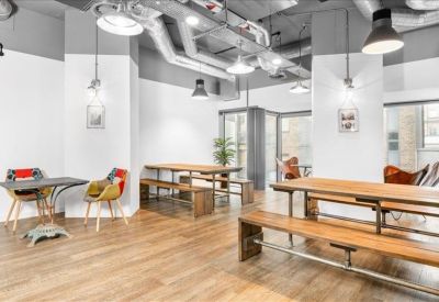 Communal breakout area with wooden picnic-style tables, benches, and warm wood flooring.