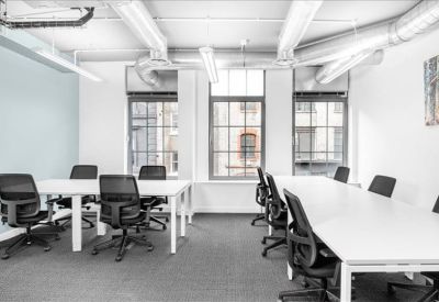 Bright open-plan office featuring white desks and black mesh chairs under industrial ceilings.