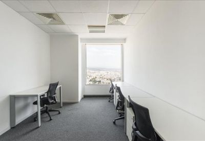 Bright multi-person office with long white desks and city views through a window.