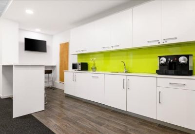 Sleek office kitchen and break area with white cabinetry and a vibrant lime green backsplash.