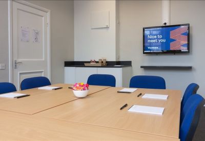 Modern meeting room with wooden table, blue chairs, and wall-mounted TV.