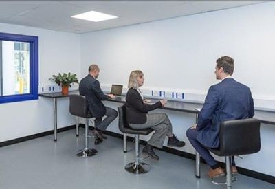 Co-working space featuring three people working at a long black desk with tall stools.