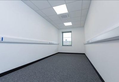 Empty private office with grey carpeting and a small window at the far end.
