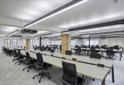 Large open-plan workspace with long white desks and black ergonomic chairs.