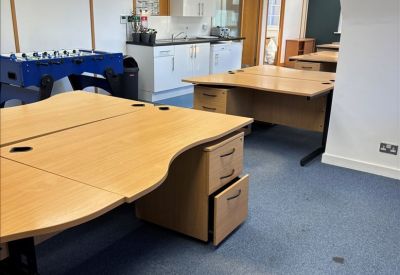 Modern office kitchen area with white cabinetry and multiple light wood desks.