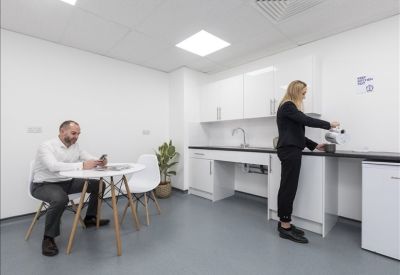 Modern communal kitchen and breakout area with a white dining table and potted plant.
