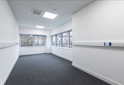 Empty open-plan office space with grey carpeting and large windows.