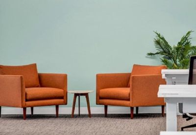 Two bright orange armchairs and a small side table against a pale green wall with a potted plant.