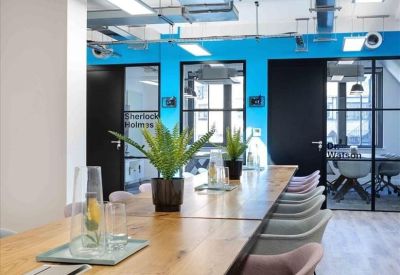 Long wooden coworking table with potted ferns and modern grey and pink seating.