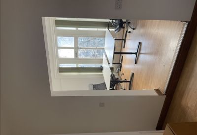 Bright office view through a wide doorway showing two desks and large windows.