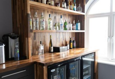 Communal bar area featuring wooden cabinetry, spirits on glass shelves, and drink coolers.