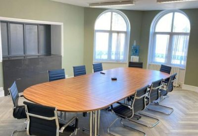 Spacious meeting room with a large wooden oval table, black chairs, and arched windows.