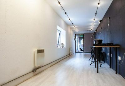 Narrow modern office space with white walls, black accent wall, and track lighting.