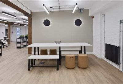 Breakout area featuring a long white communal table, wooden stools, and decorative circular wall lights.
