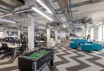 Open-plan coworking space with a chevron carpet, foosball table, and blue breakout seating.