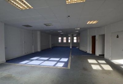 Large empty office suite with blue carpet and natural light from rear windows.