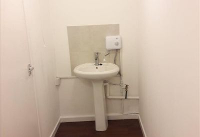 Compact kitchenette or wash area with a white pedestal sink and dark wood-effect flooring.