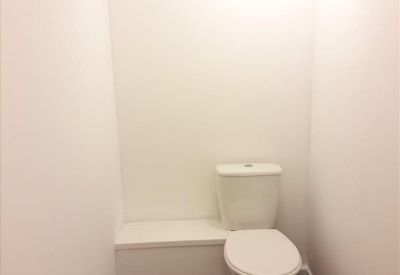 Private restroom featuring a white toilet and dark wood-style flooring.