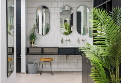 Contemporary restroom with oval mirrors, white tiling, and an orange stool.