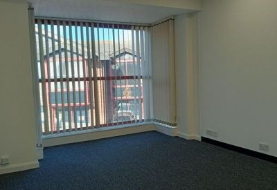 Bright corner office space with blue carpet and large windows with vertical blinds.