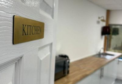 Kitchen doorway featuring a gold-toned sign and white door leading to a modern break area.