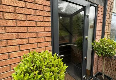 Modern glass entrance door with dark frames and potted topiary trees.
