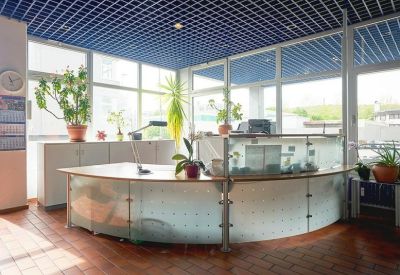 Curved glass reception desk under a blue grid ceiling with potted plants.