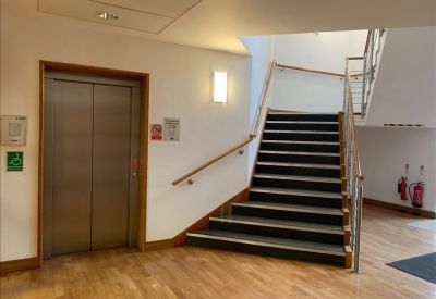 Modern building lobby with an elevator, wooden flooring, and a staircase with metal railings.