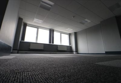 Spacious, empty office room with grey patterned carpet and large windows providing natural light.
