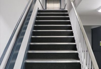 Internal staircase with dark grey carpet and white metal railings leading towards an elevator.