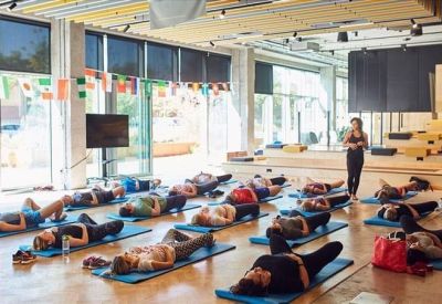 Spacious communal space with people practicing yoga on mats by large windows.