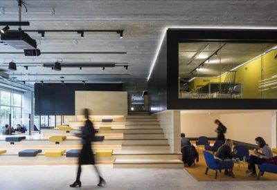 Large breakout area with tiered stadium seating, blue armchairs, and a modern mezzanine.
