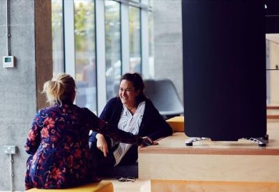 Two women talking in a bright breakout space near a large window.